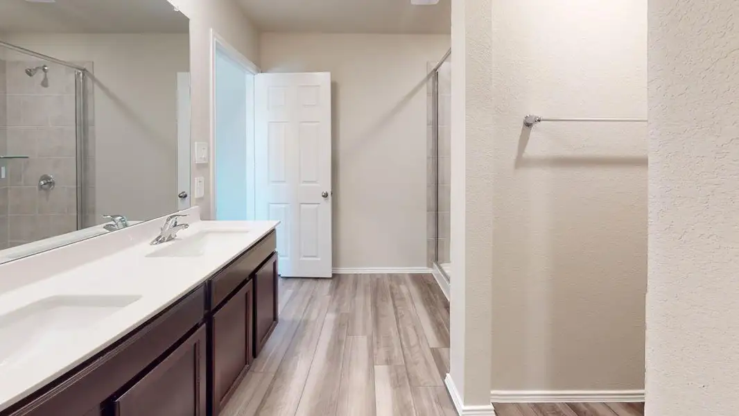 Full bathroom with double vanity, light wood-style flooring, and a shower stall