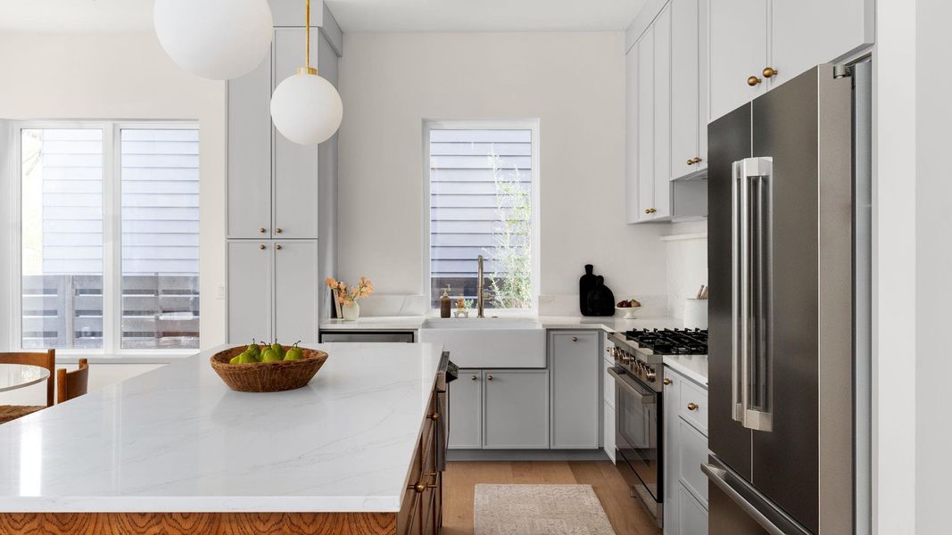 Kitchen featuring high end appliances, light stone counters, light wood-style floors, a center island, and hanging light fixtures