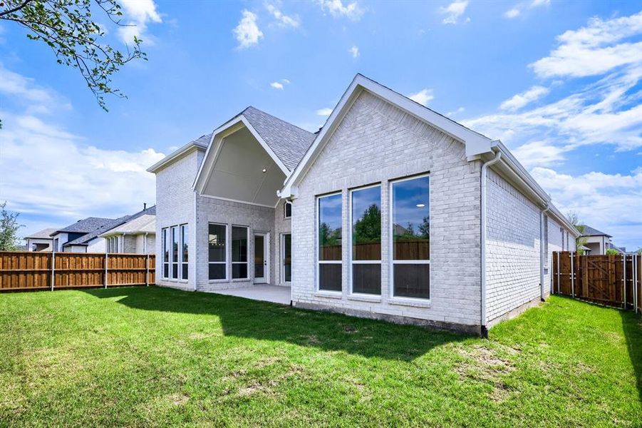 Spacious backyard featuring a manicured lawn, a light-colored brick exterior, a covered patio, and large windows Spacious backyard featuring a manicured lawn, a light-colored brick exterior, a covered patio, and large windows