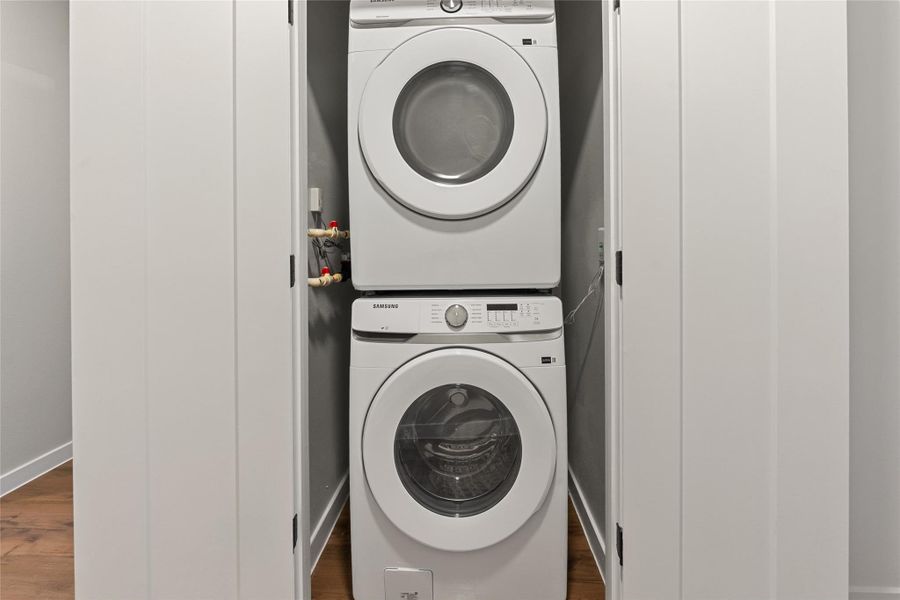 Laundry room featuring stacked washing machine and dryer and dark wood finished floors