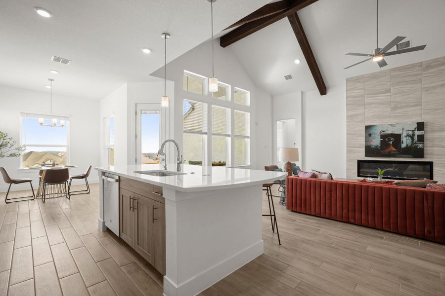 An open concept living area boasts vaulted ceilings, a central kitchen island, and a sleek fireplace.