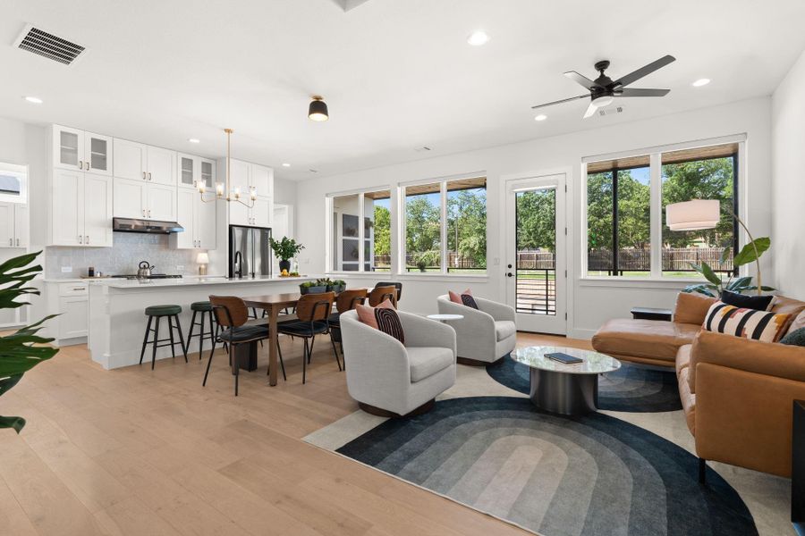 This photo showcases a bright, open-concept living space featuring a modern kitchen with white cabinetry and stainless steel appliances. There's a spacious island with bar seating and an adjacent dining area. The living area includes large windows offering plenty of natural light and stunning views.
