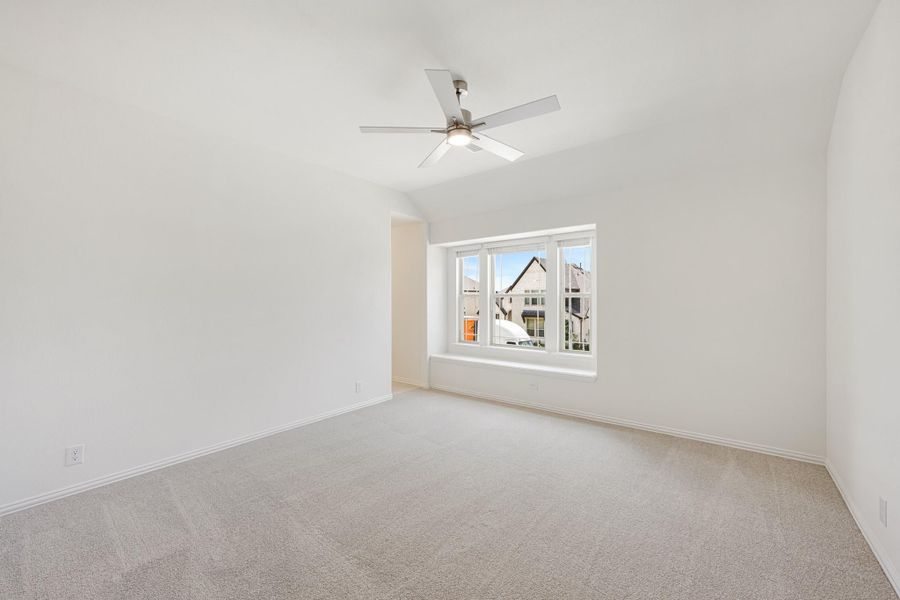 Empty bedroom with vaulted ceiling, ceiling fan, carpet flooring, and large window with neighborhood view Empty bedroom with vaulted ceiling, ceiling fan, carpet flooring, and large window with neighborhood view