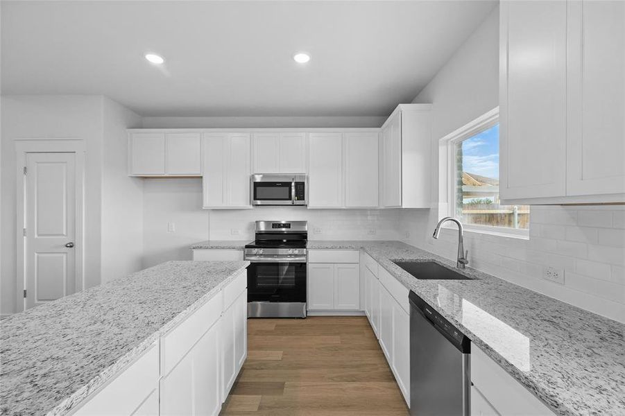 Kitchen featuring appliances with stainless steel finishes, a sink, white cabinetry, light stone counters, and light wood finished floors Kitchen featuring appliances with stainless steel finishes, a sink, white cabinetry, light stone counters, and light wood finished floors