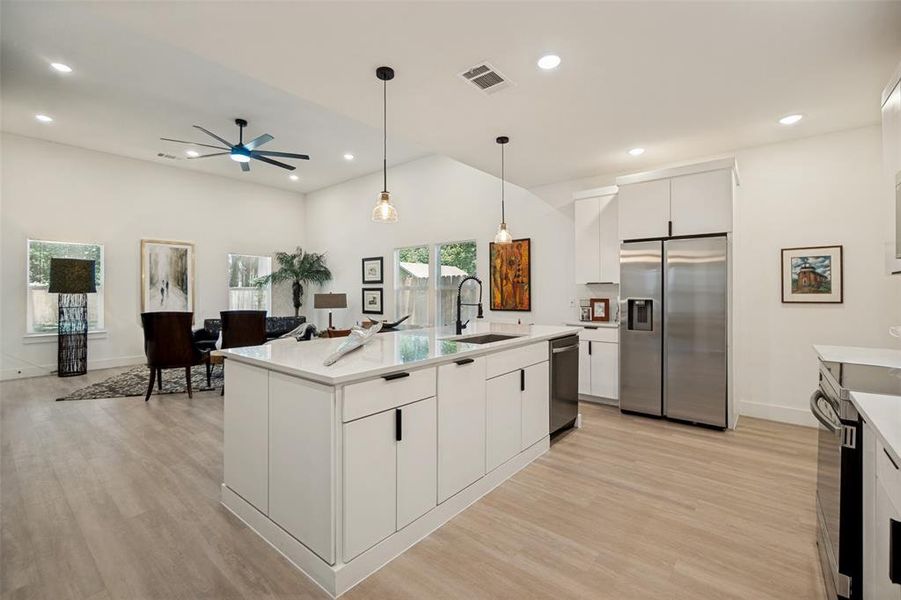 Contemporary kitchen featuring a large center island with integrated sink, white cabinetry with matte black hardware, stainless steel appliances, and light wood-finish flooring Contemporary kitchen featuring a large center island with integrated sink, white cabinetry with matte black hardware, stainless steel appliances, and light wood-finish flooring