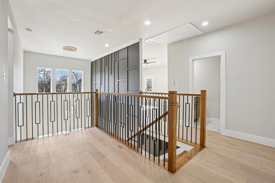 Corridor with an upstairs landing, light wood finished floors, and recessed lighting