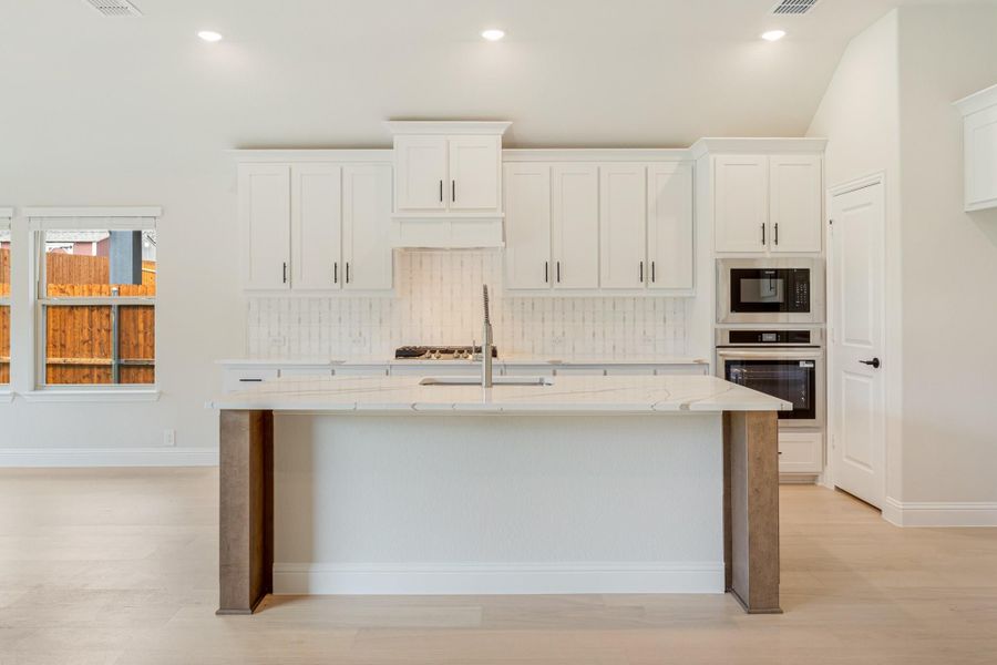 Kitchen with large island, white cabinets, quartz countertops, tile backsplash, and stainless steel double oven Kitchen with large island, white cabinets, quartz countertops, tile backsplash, and stainless steel double oven