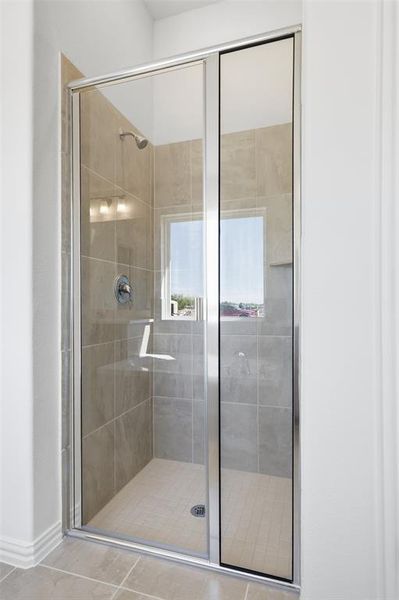 Enclosed shower with clear glass door, tiled walls, built-in shelf, frosted window, and overhead lighting