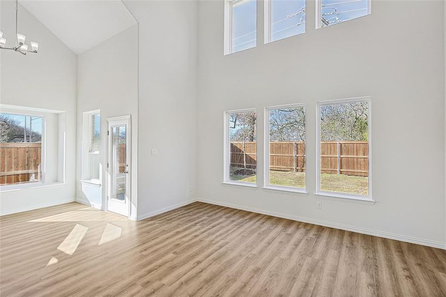 Unfurnished living room with light wood-type flooring, a high ceiling, and an inviting chandelier