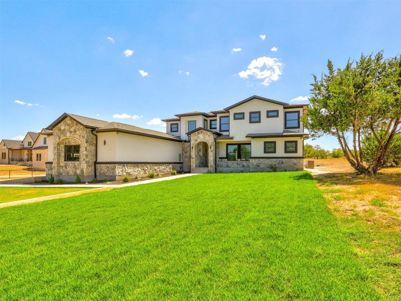 An expansive green lawn leads to a grand two-story estate showcasing beautiful stone masonry accent walls.