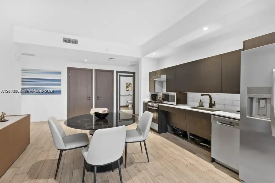 Contemporary kitchen featuring flat-panel cabinetry, stainless steel appliances, subway tile backsplash, recessed lighting, and wood-finish flooring Contemporary kitchen featuring flat-panel cabinetry, stainless steel appliances, subway tile backsplash, recessed lighting, and wood-finish flooring