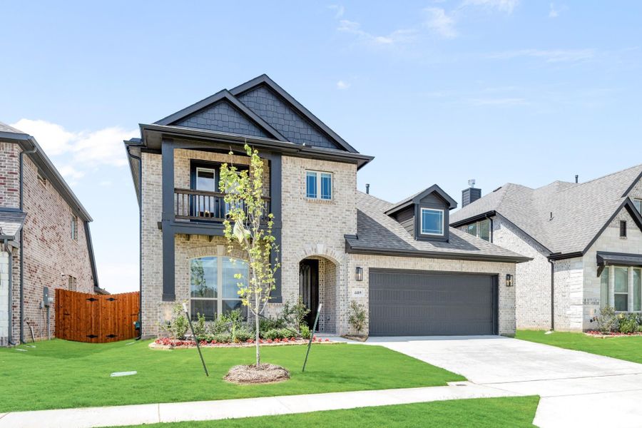 Two-story brick home with second-floor balcony, two-car garage, and manicured front lawn