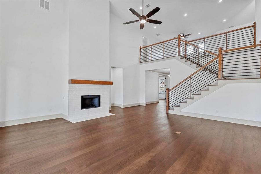 Unfurnished living room featuring a high ceiling, wood-type flooring, a brick fireplace, and ceiling fan