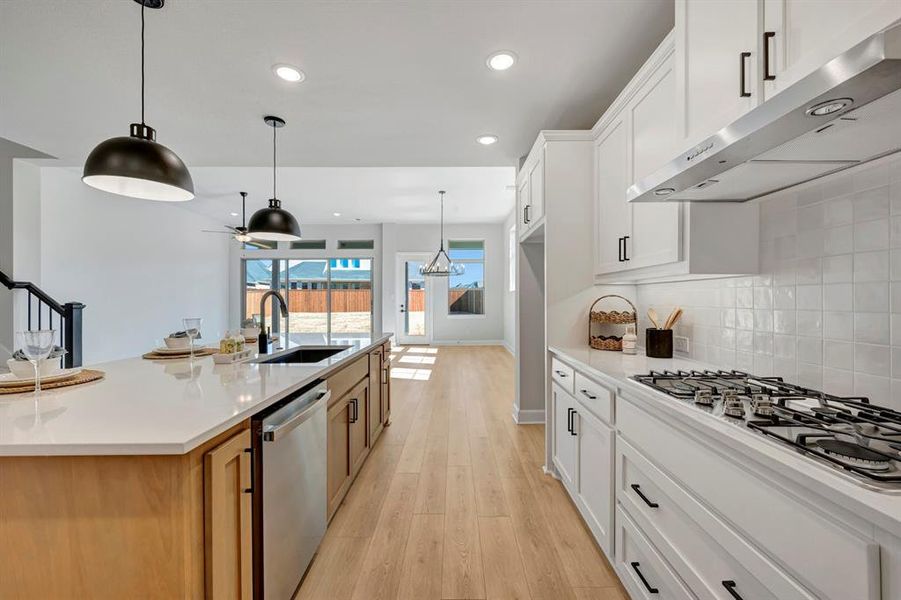 Kitchen featuring light wood finished floors, stainless steel appliances, hanging light fixtures, a large island, and light stone counters