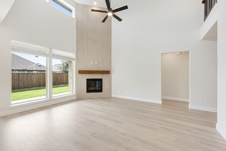 Open living room with two-story ceiling, tile fireplace, ceiling fan, and light wood floors