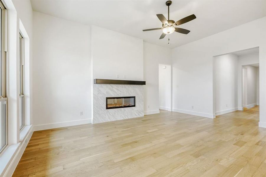 Unfurnished living room with a ceiling fan, light wood-type flooring, and a fireplace