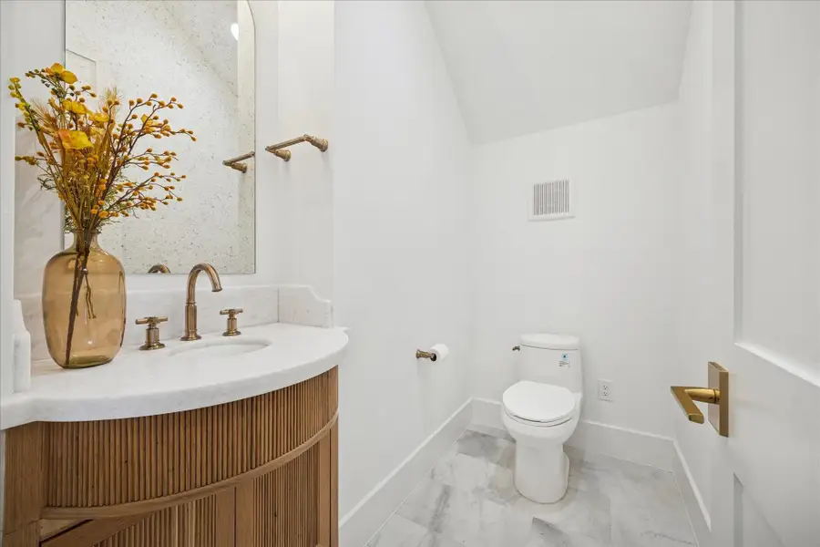 Soft neutral tones, quartz vanity, brass plumbing, and vertically stacked tile create a quiet architectural moment. Spray foam insulation maintains temperature and reduces sound transmission.