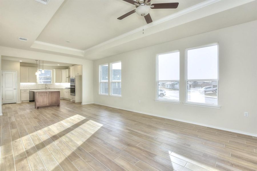 Unfurnished living room with visible vents, light wood-type flooring, a raised ceiling, and ceiling fan