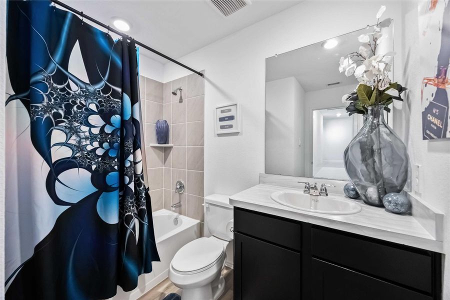 This modern bathroom features a design with a tiled bathtub, and a vanity with a large mirror.