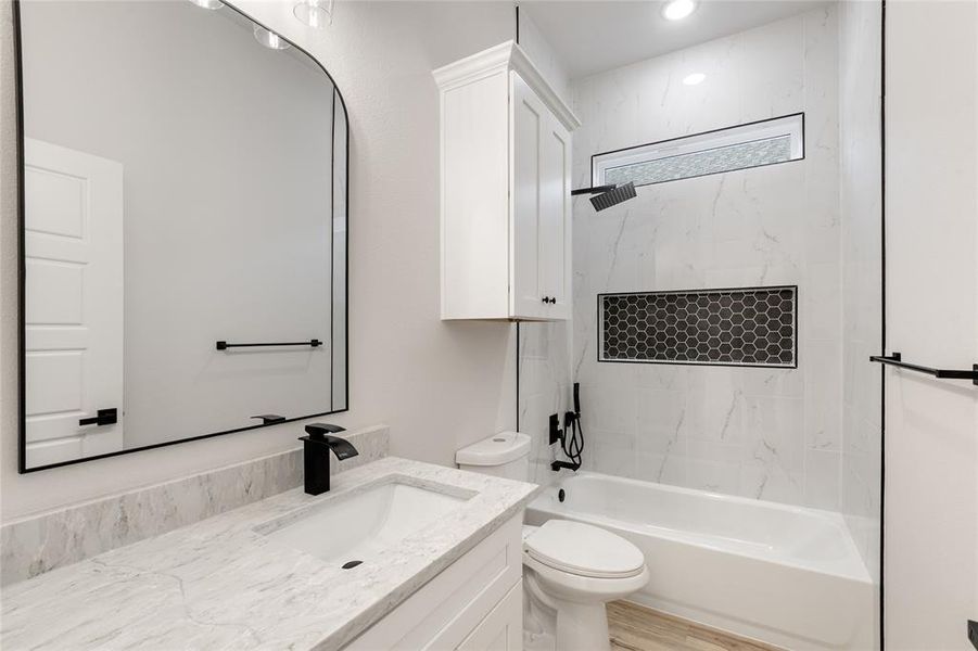 Full bathroom between the two front bedrooms, featuring vanity, tub/shower combination, and wood-finished floors.
