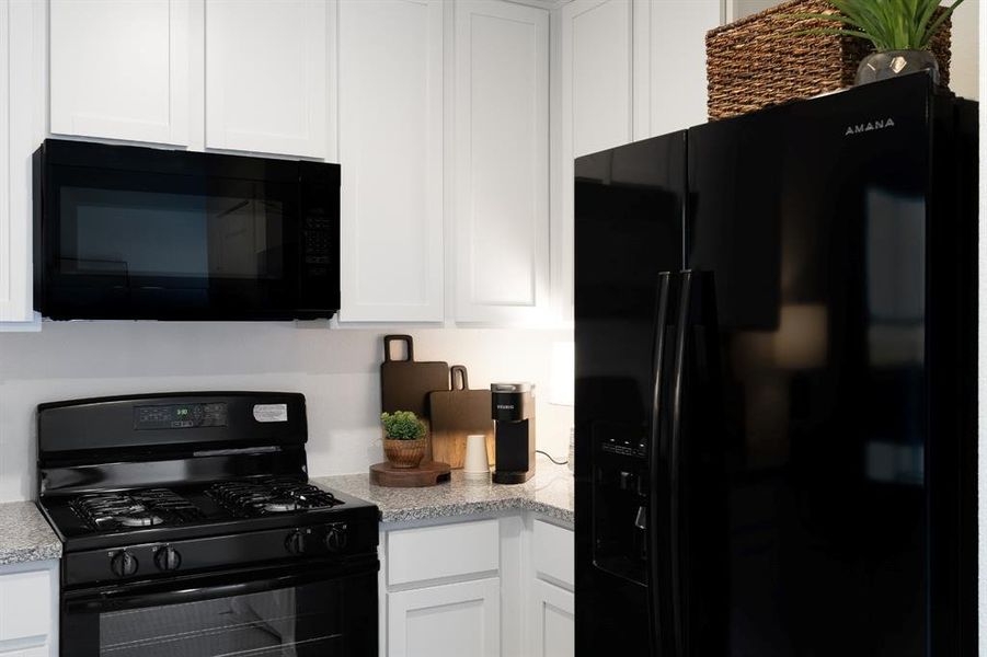 Kitchen with black appliances, white cabinetry, and light stone counters