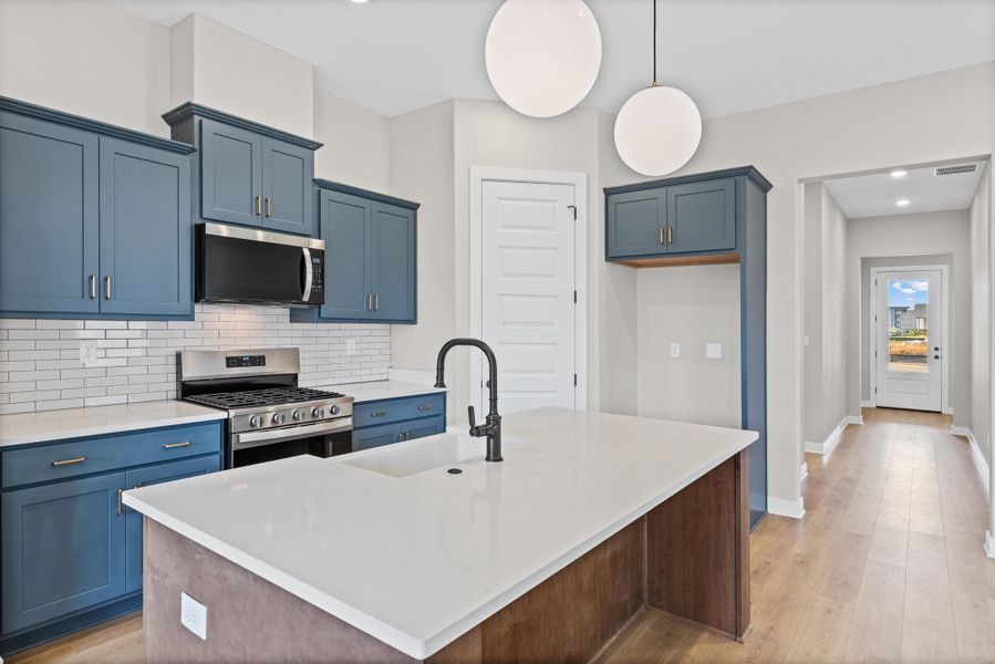Contemporary kitchen featuring blue shaker-style cabinetry, white subway tile backsplash, stainless steel gas range, and a large central island with white countertop and black faucet Contemporary kitchen featuring blue shaker-style cabinetry, white subway tile backsplash, stainless steel gas range, and a large central island with white countertop and black faucet