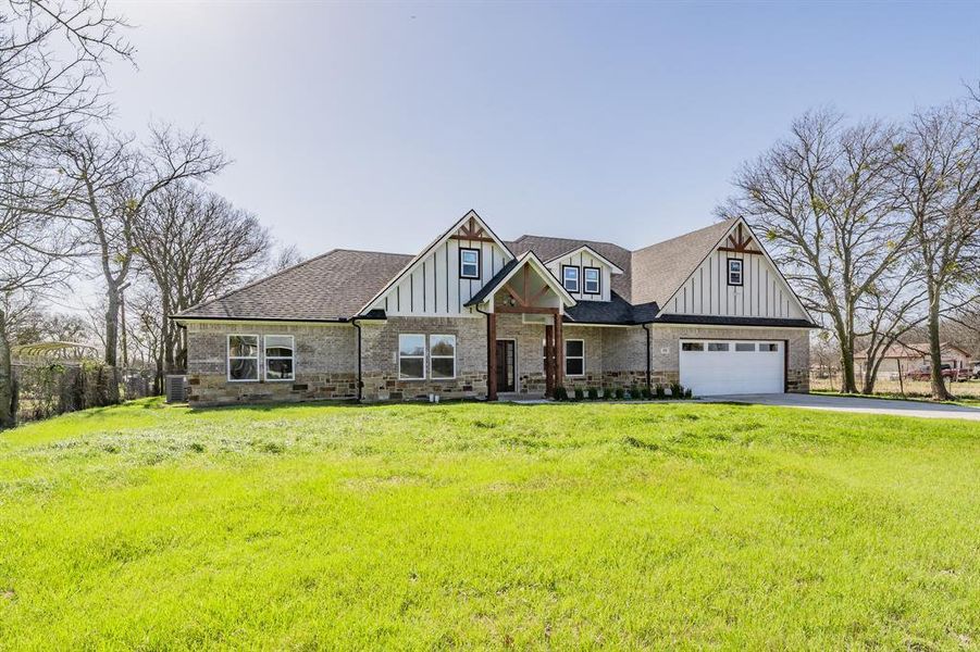 View of front of property featuring brick siding, roof with shingles, an attached garage, board and batten siding, and driveway