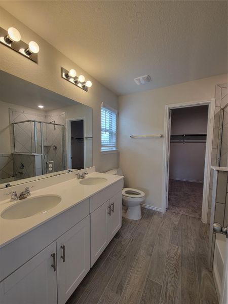 Full bathroom with a walk in closet, a shower stall, double vanity, dark wood finished floors, and a textured ceiling