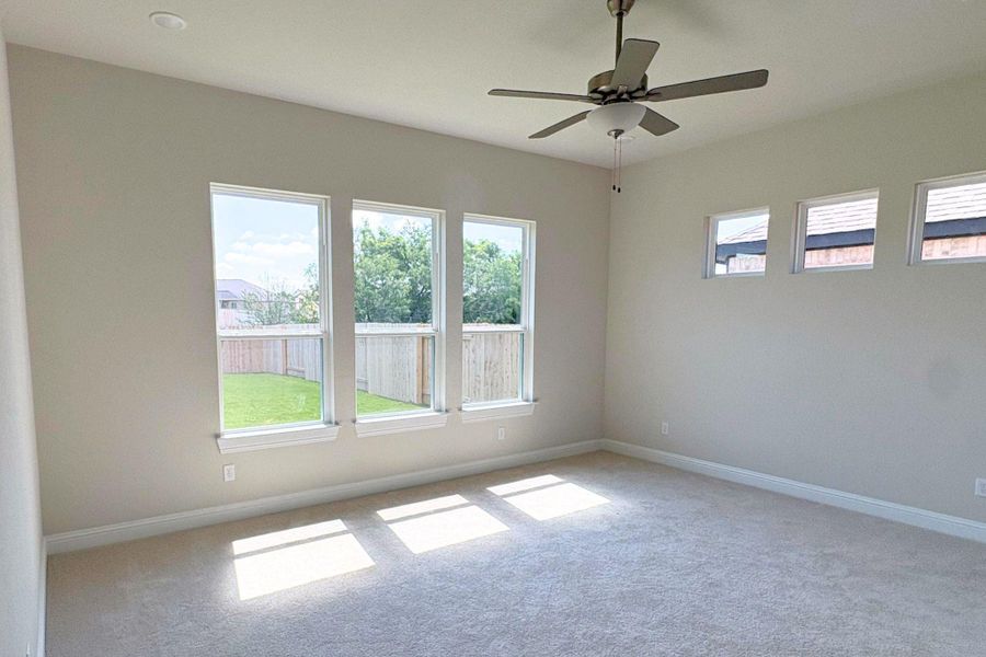 Spacious room featuring neutral carpeting, a ceiling fan, and multiple windows providing natural illumination