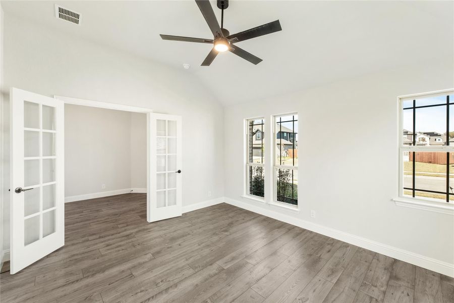 Empty room with hardwood floors, vaulted ceiling, ceiling fan, and French doors
