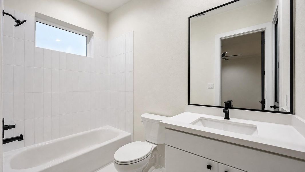 The adjoining full bathroom continues the home’s crisp black-and-white aesthetic with a streamlined vanity, black-framed mirror, matte black faucet, and a tub/shower combination surrounded by glossy white tile. A horizontal window introduces natural light while maintaining privacy. Clean lines and neutral finishes create a fresh, functional space with contemporary appeal. The adjoining full bathroom continues the home’s crisp black-and-white aesthetic with a streamlined vanity, black-framed mirror, matte black faucet, and a tub/shower combination surrounded by glossy white tile. A horizontal window introduces natural light while maintaining privacy. Clean lines and neutral finishes create a fresh, functional space with contemporary appeal.
