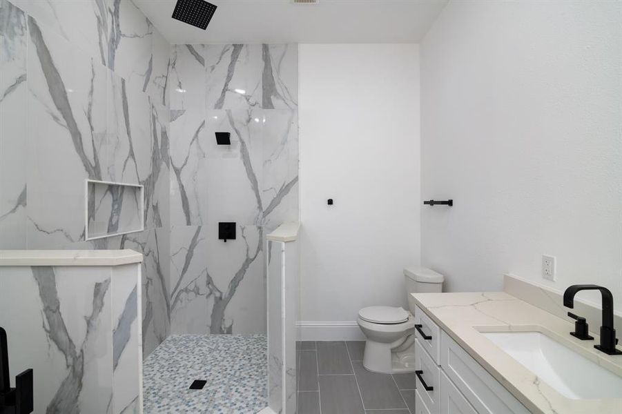 Bathroom with toilet, vanity, tile patterned floors, and tiled shower