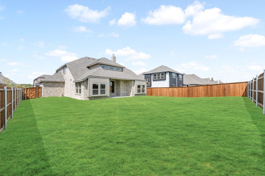 Brick home rear exterior with large fenced backyard and green lawn in a suburban neighborhood