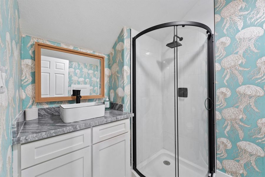 This fifth full bathroom located off the flex room features a modern shower with a glass door, a stylish vanity with a vessel sink, and vibrant Serena & Lily jellyfish-themed wallpaper, creating a unique, fun  and inviting space. The perfect finish to the flex space.