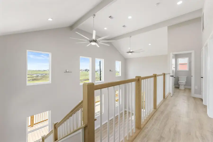 Bright and airy upper hallway with large windows offering scenic views, high ceilings with ceiling fans, light wood flooring, and a view into a bathroom. Bright and airy upper hallway with large windows offering scenic views, high ceilings with ceiling fans, light wood flooring, and a view into a bathroom.