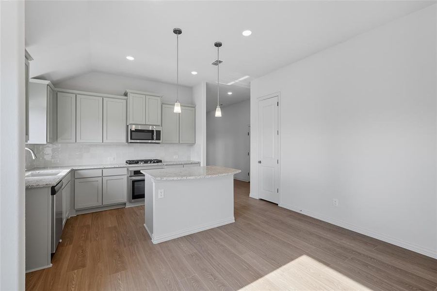 Kitchen with decorative backsplash, decorative light fixtures, light wood finished floors, appliances with stainless steel finishes, and light stone countertops Kitchen with decorative backsplash, decorative light fixtures, light wood finished floors, appliances with stainless steel finishes, and light stone countertops