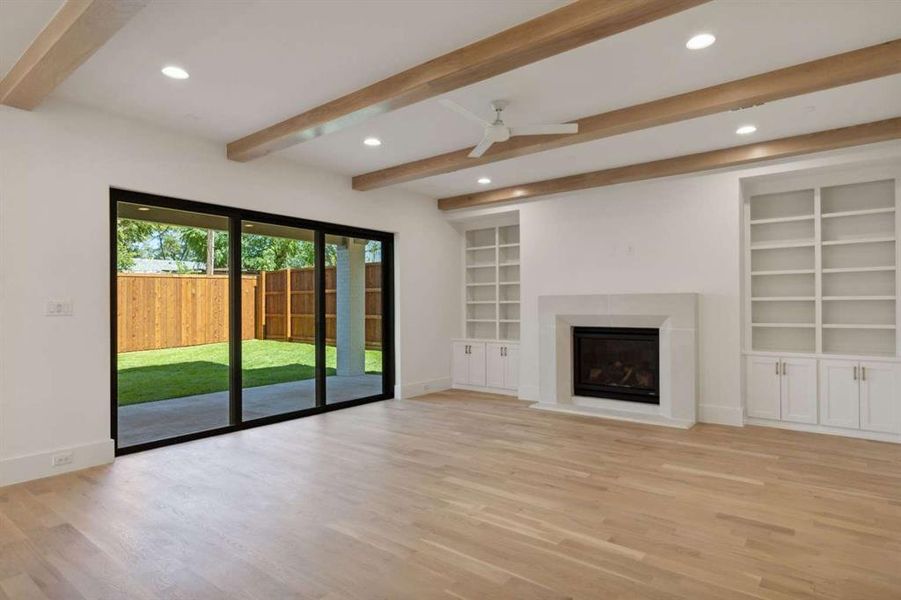 Unfurnished living room featuring ceiling fan, light hardwood / wood-style flooring, beam ceiling, and built in shelves