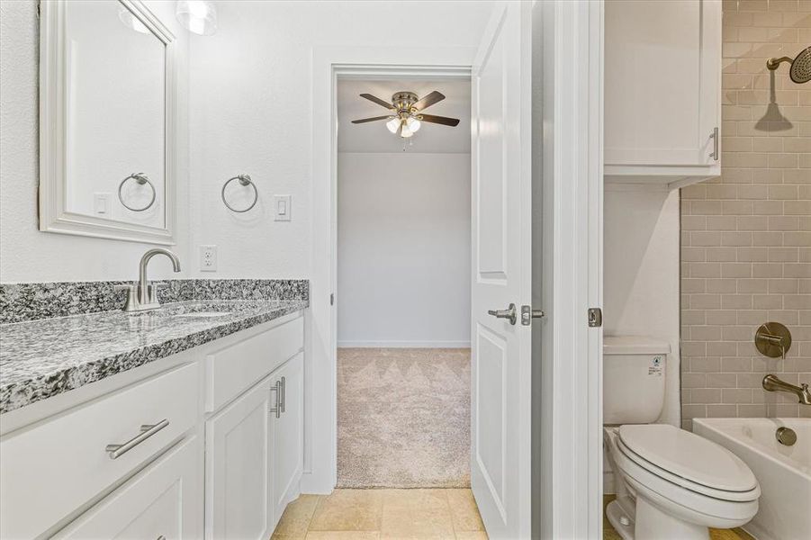 Full bathroom with ceiling fan, tiled shower / bath combo, tile patterned flooring, toilet, and vanity Full bathroom with ceiling fan, tiled shower / bath combo, tile patterned flooring, toilet, and vanity
