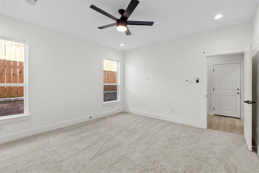 Empty room with ceiling fan, a wealth of natural light, and light carpet