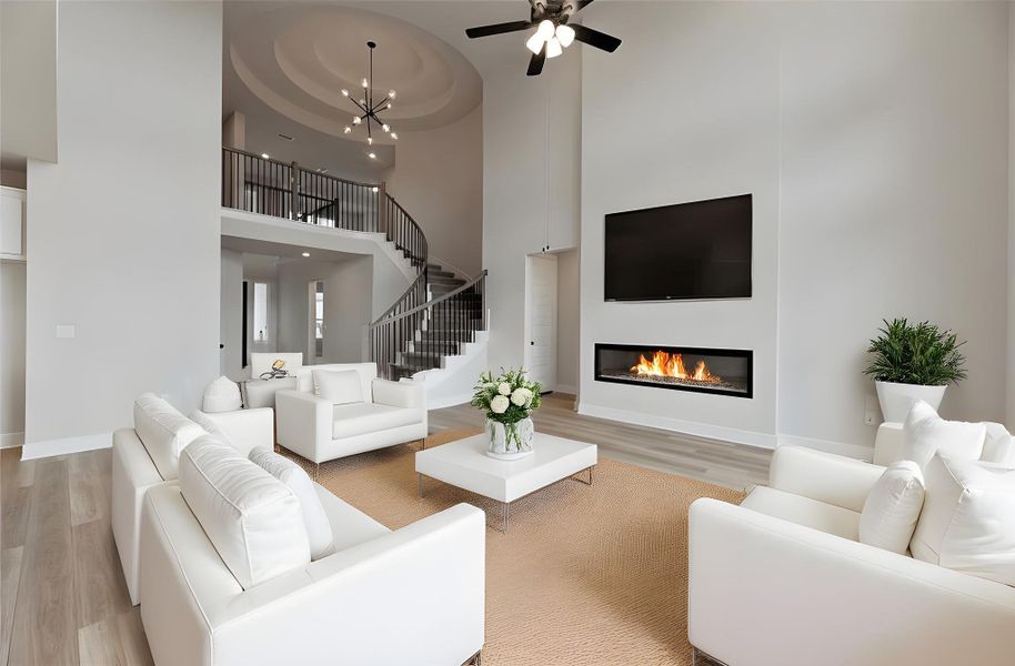Living room with a glass covered fireplace, a high ceiling, light wood finished floors, a ceiling fan, and stairway