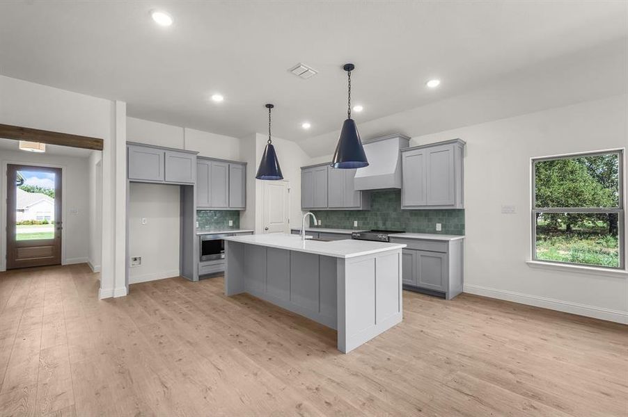 Kitchen with gray cabinets, tasteful backsplash, light floors, a kitchen island with sink, and a breakfast bar