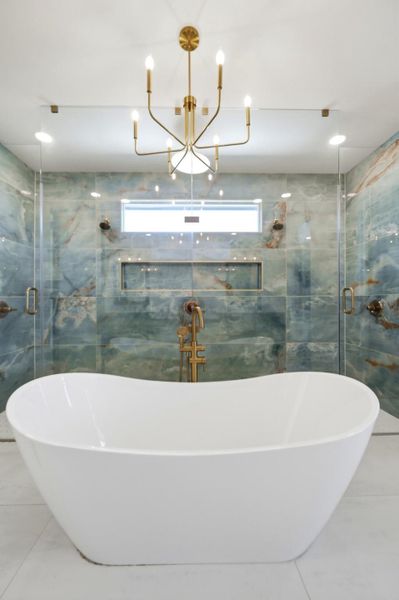 An elegant freestanding soaking tub rests before a custom tiled walk-in shower.