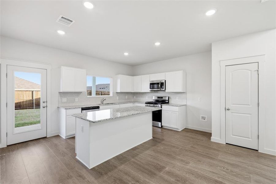 Kitchen featuring an island with granite countertops, white cabinetry, stainless steel appliances, and wood-finish flooring Kitchen featuring an island with granite countertops, white cabinetry, stainless steel appliances, and wood-finish flooring