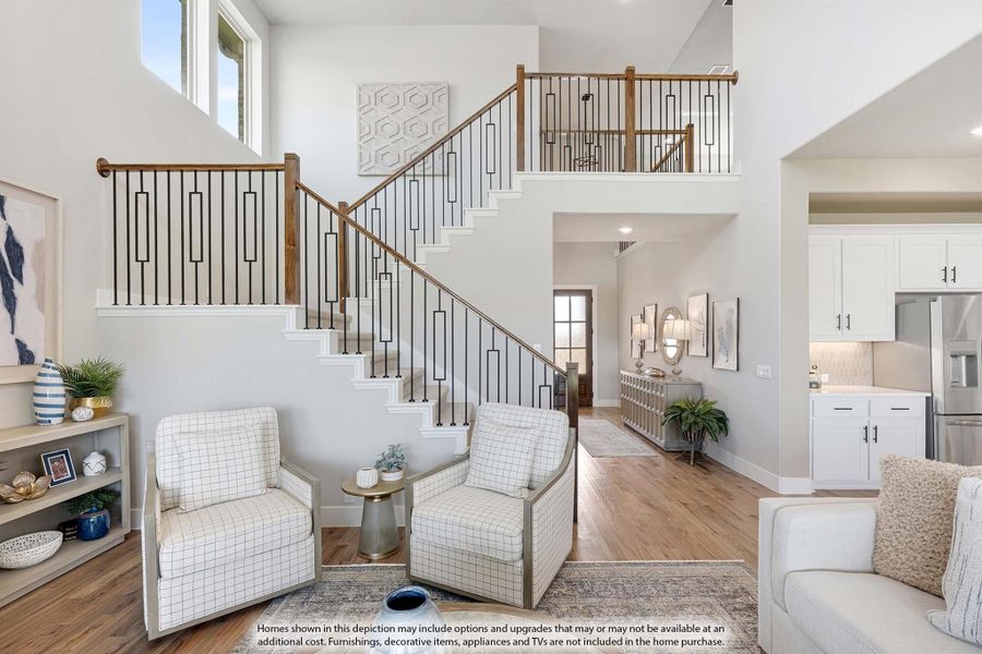 Two-story living room with wood and iron staircase, hardwood floors, and open view to kitchen