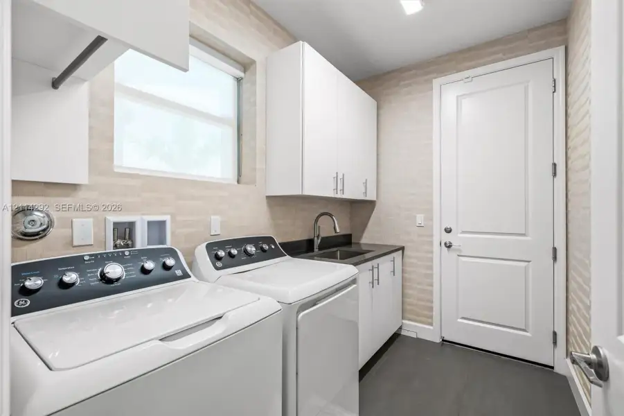 Utility room featuring textured wall tile, white shaker-style cabinetry, a dark countertop with a built-in sink, and slate-finish flooring