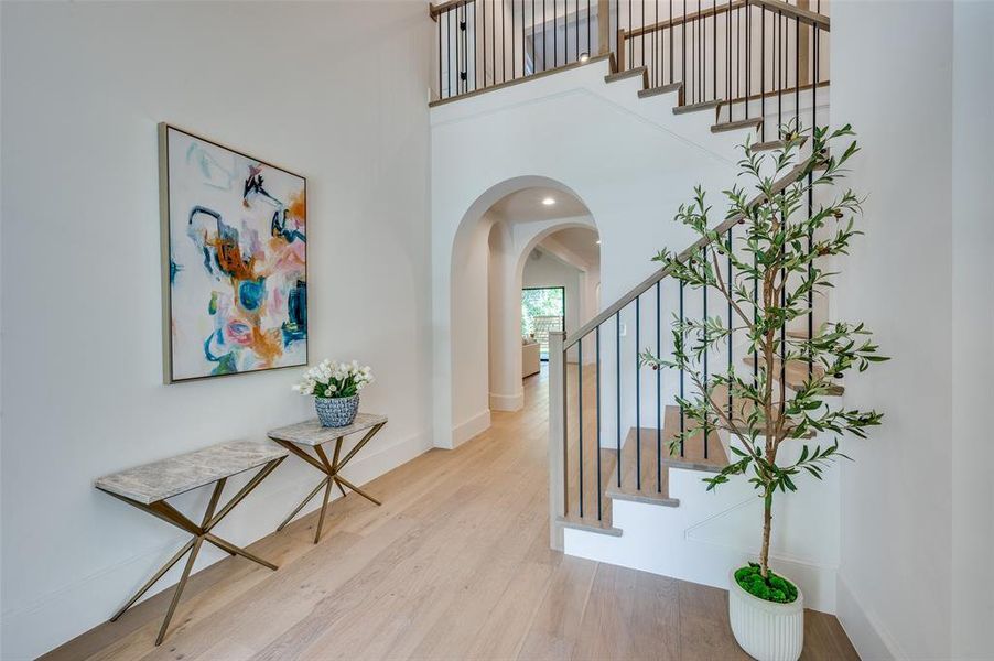 Foyer with wood finished floors, stairs, arched walkways, and a towering ceiling