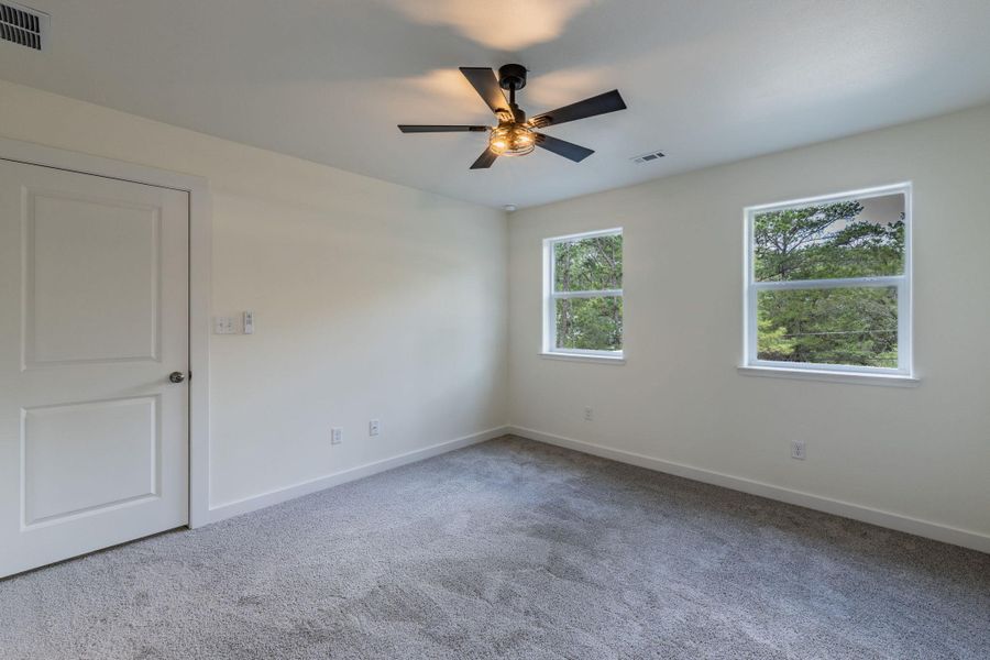 Spacious room with plush gray carpeting, two large windows, a ceiling fan with integrated lighting, a white panel door, and neutral wall tones Spacious room with plush gray carpeting, two large windows, a ceiling fan with integrated lighting, a white panel door, and neutral wall tones