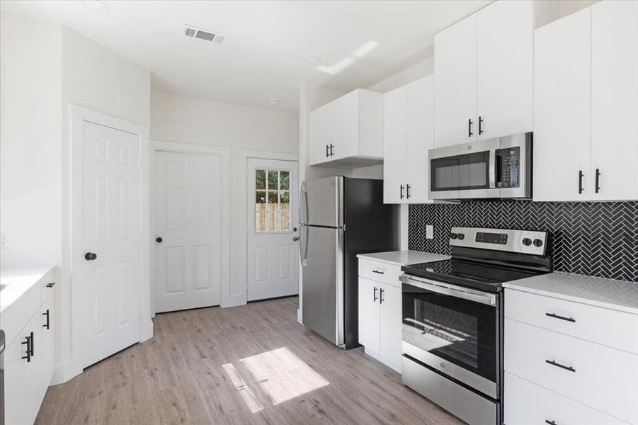 Kitchen featuring appliances with stainless steel finishes, light hardwood / wood-style floors, backsplash, and white cabinetry