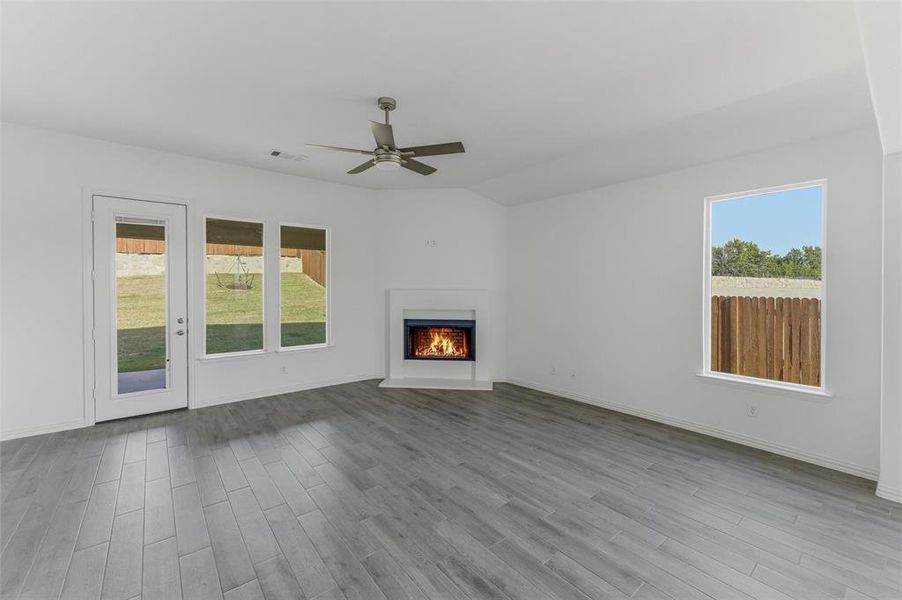 Unfurnished living room featuring a ceiling fan, a lit fireplace, light wood finished floors, and vaulted ceiling