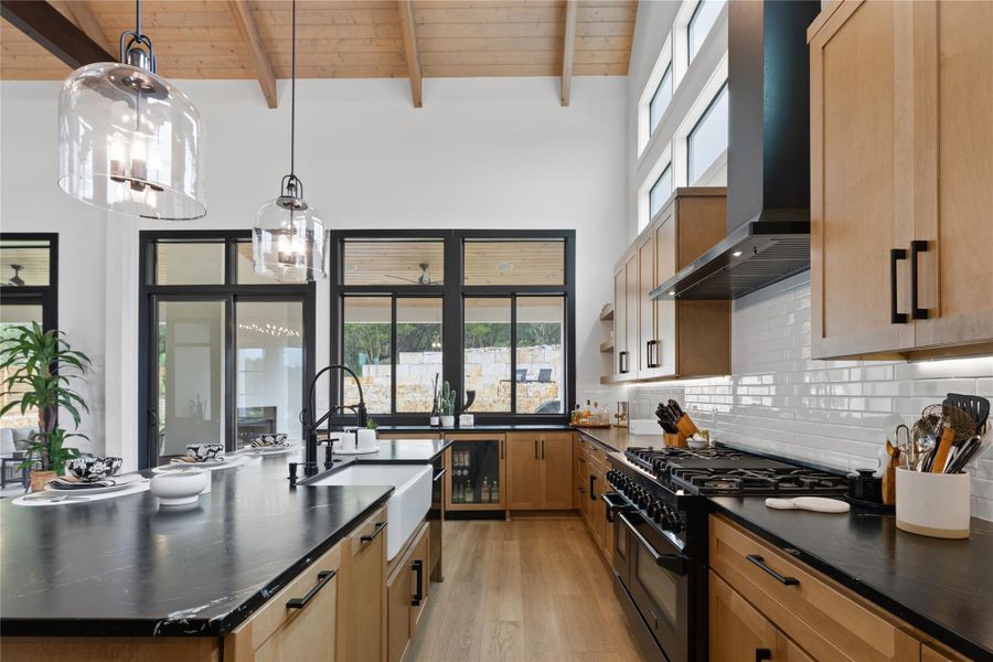Spacious kitchen featuring light wood cabinetry, black countertops, a large farmhouse sink, and a black range with coordinating hood Spacious kitchen featuring light wood cabinetry, black countertops, a large farmhouse sink, and a black range with coordinating hood